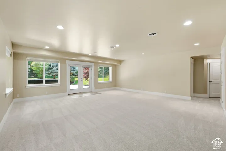 Recessed lighting illuminates the expansive carpeted room with multiple windows and a double glass door
