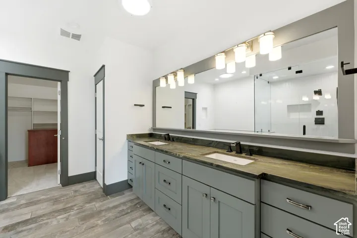 Dual vanity with integrated sinks, stone countertop, wood-finish flooring, full-width mirror, and enclosed shower with glass panels
