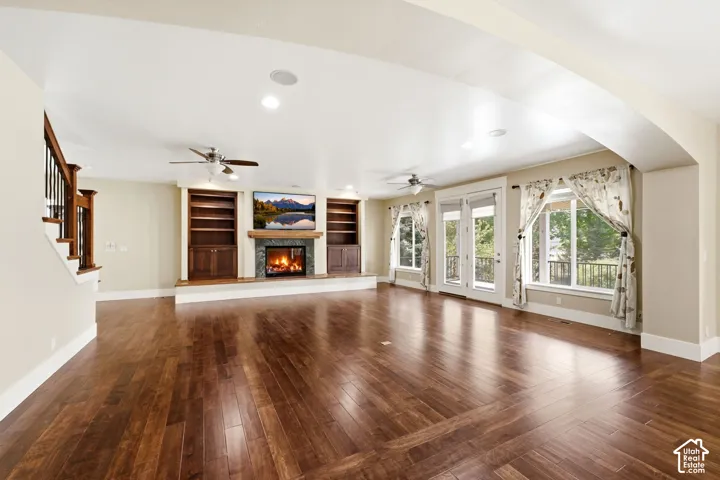 Wide-plank wood-finish flooring, built-in cabinetry with shelving, a tiled fireplace with wood mantel, multiple ceiling fans, and double French doors to an exterior space