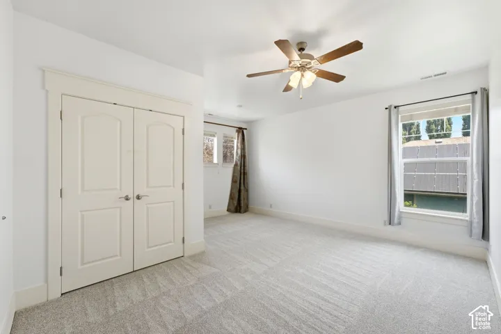 Light gray carpet flooring, white walls, white trim, a ceiling fan, and a double-door closet