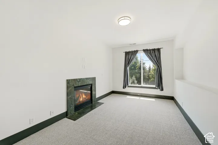 Built-in fireplace with a stone surround, carpeted flooring, and a flush-mount ceiling light
