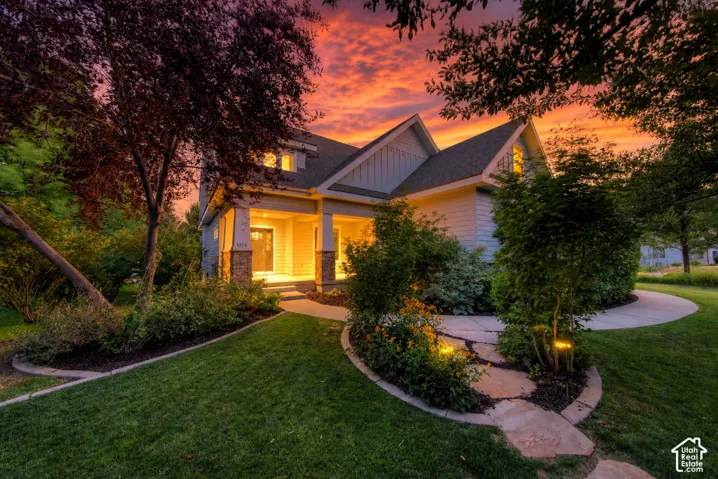 Gabled roofline, covered porch with stone columns, landscaped grounds, winding pathway with flagstone accents, and integrated exterior lighting