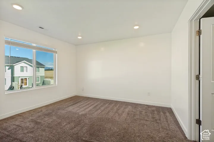 Recessed ceiling lighting, white walls, brown carpet flooring, and a window with blinds