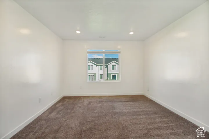 Recessed lighting illuminates this room featuring light-colored walls and brown carpeting