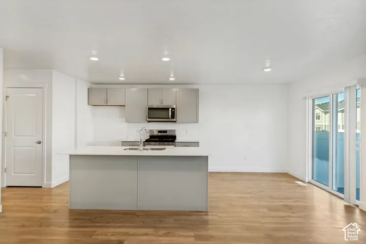 Open-concept living area featuring wood-finish flooring, a kitchen island with a sink, stainless steel appliances, and a sliding glass door