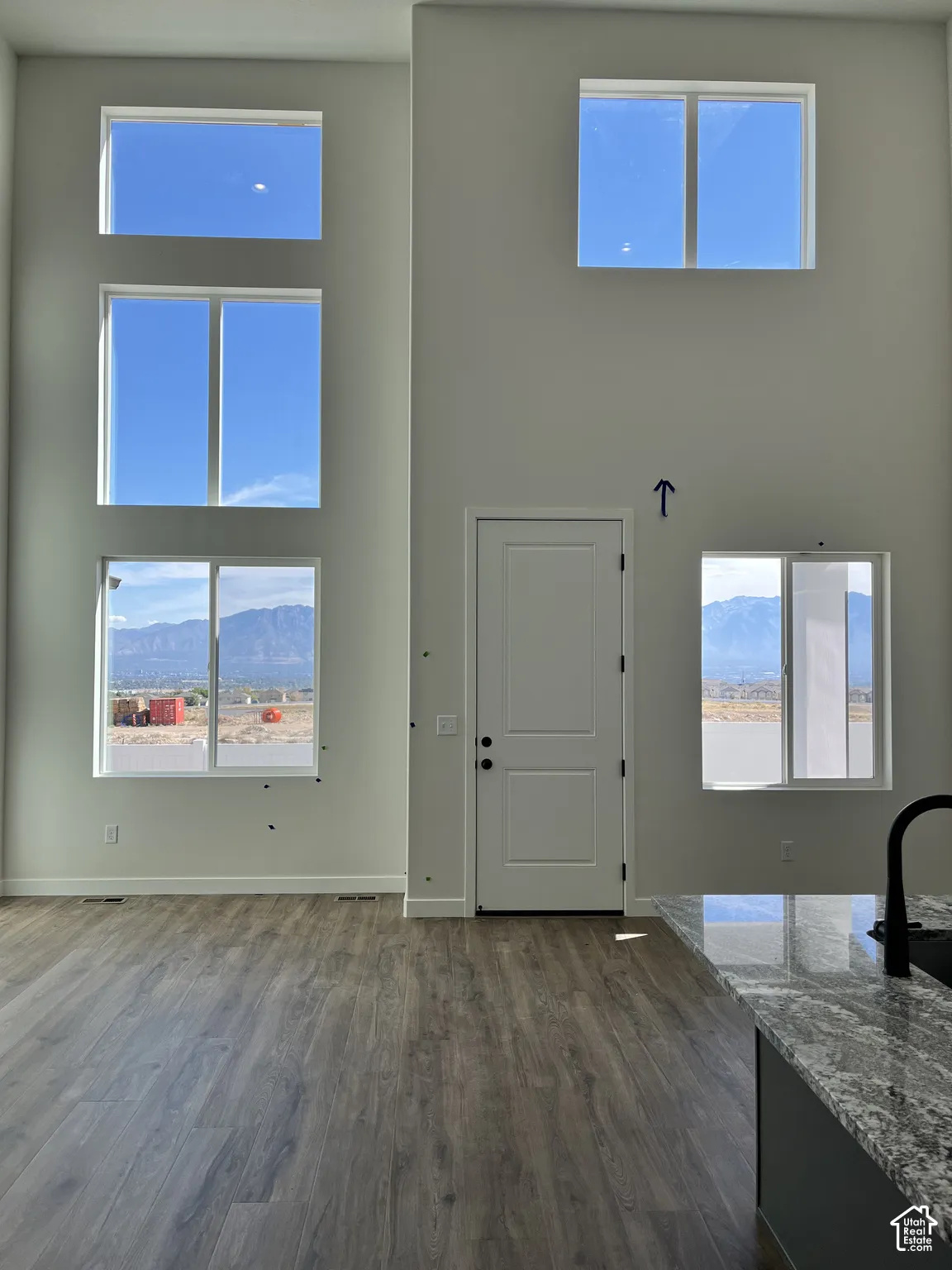 Two-story living area featuring tall windows, wood-finish flooring, and a kitchen island with a granite countertop