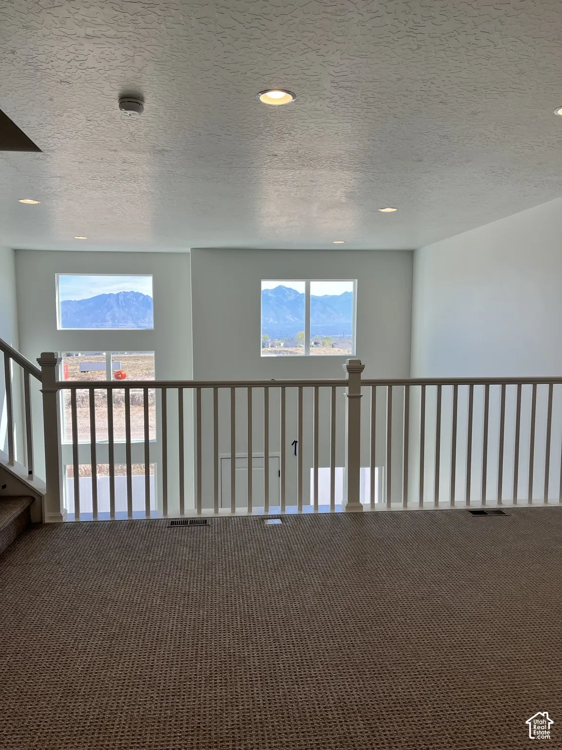 Carpeted open loft area with white baluster railing and recessed ceiling lighting