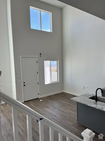 Vaulted ceiling with high windows, wood-finish flooring, white paneled door, kitchen island with granite countertop, and black sink fixture