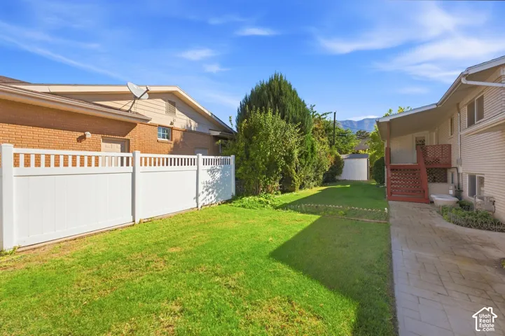 Expansive green lawn, white privacy fencing, brick exterior, paved walkway, and mountain backdrop
