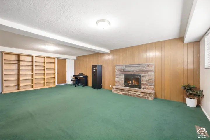 Integrated shelving system, stone-clad fireplace with hearth, wood paneling, and carpeted flooring