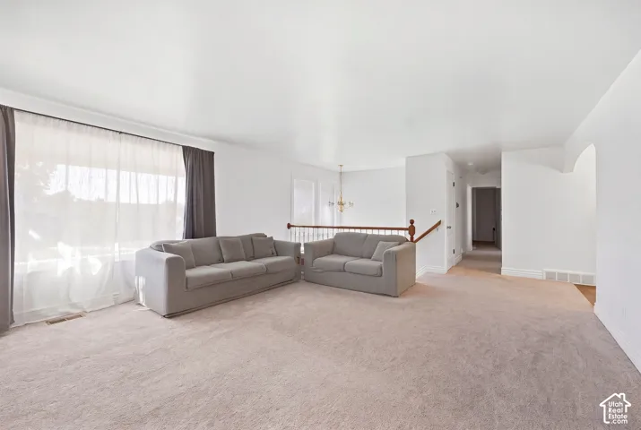 Spacious carpeted room featuring a large window, white walls, and a wooden handrail with balusters