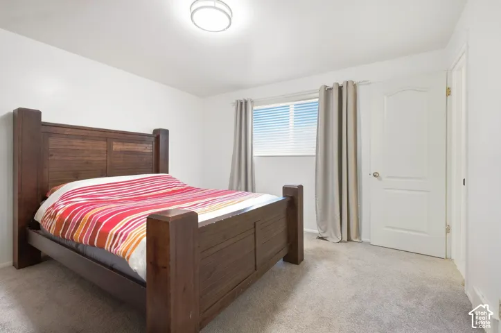Recessed window with horizontal blinds, light gray wall-to-wall carpeting, white interior door with arched paneling, and a flush mount ceiling light fixture