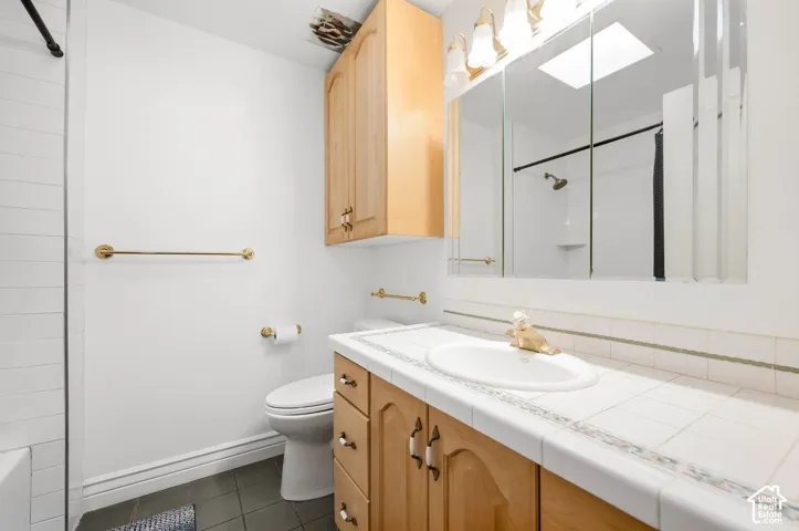 Bathroom featuring a wood-finish vanity with a tile countertop, integrated sink, and a mirrored medicine cabinet