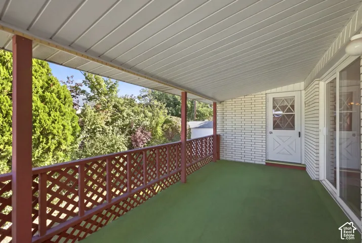 Covered porch with green flooring, white brick-patterned siding, red lattice railing, and a white paneled door with window accents