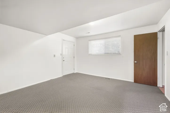 Room with light gray patterned carpeting, white walls, a white paneled door, a window with horizontal blinds, and a wood-finish door