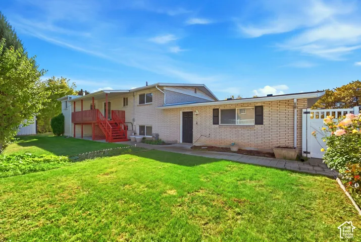 Expansive grassy yard with a white picket fence, brick exterior, and a red wood-finish deck with stairs