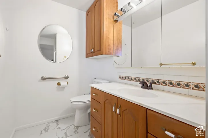 White marble-look flooring, wood-finish vanity with countertop, medicine cabinet, and wall-mounted storage cabinet