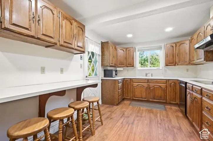 U-shaped kitchen with wood-finish flooring, ample wood cabinetry, white countertops, and a built-in breakfast bar