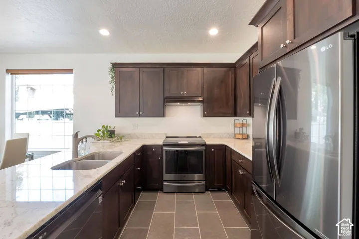 U-shaped kitchen featuring dark wood cabinetry, light-toned countertops, stainless steel appliances, and a double basin sink