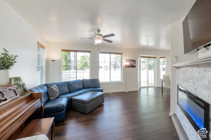Wood-finish flooring, multiple windows with natural light, ceiling fan, fireplace with stone surround, and sliding glass door