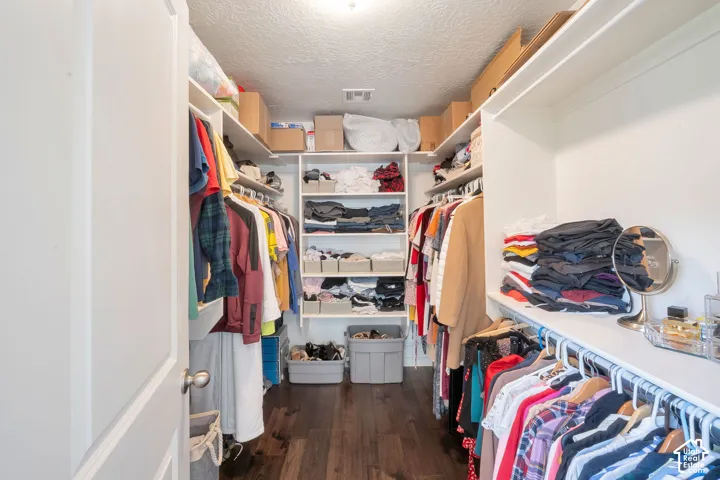 Walk-in closet featuring built-in shelving, multiple hanging rods, and dark wood-finish flooring