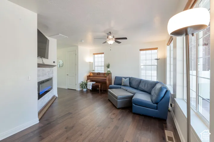 Spacious living area featuring wood-finish flooring, multiple windows, a ceiling fan, and a built-in fireplace with stone detailing