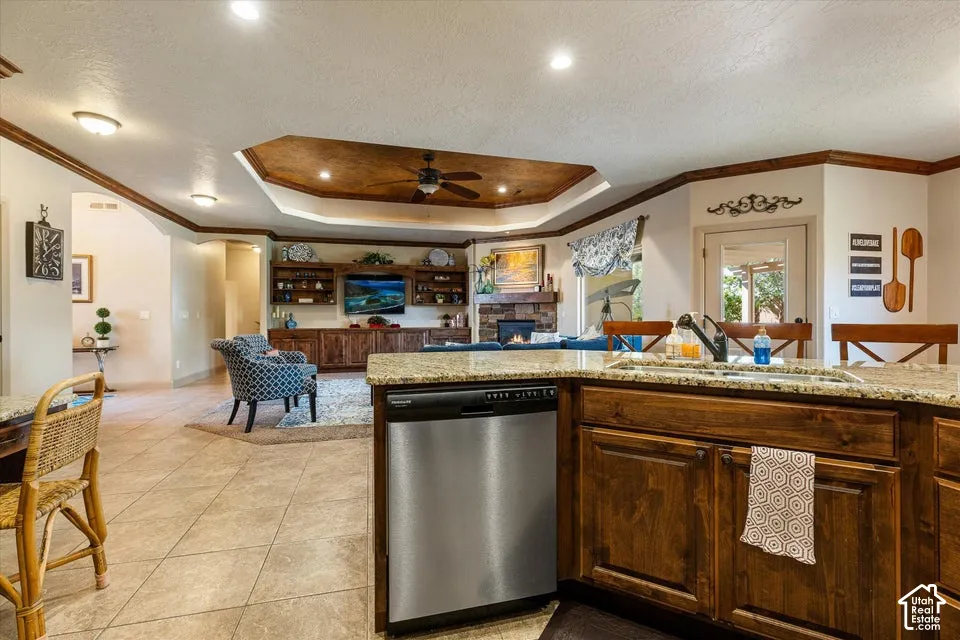 Recessed lighting, wood-finish cabinetry, stainless steel dishwasher, tile flooring, and a decorative tray ceiling