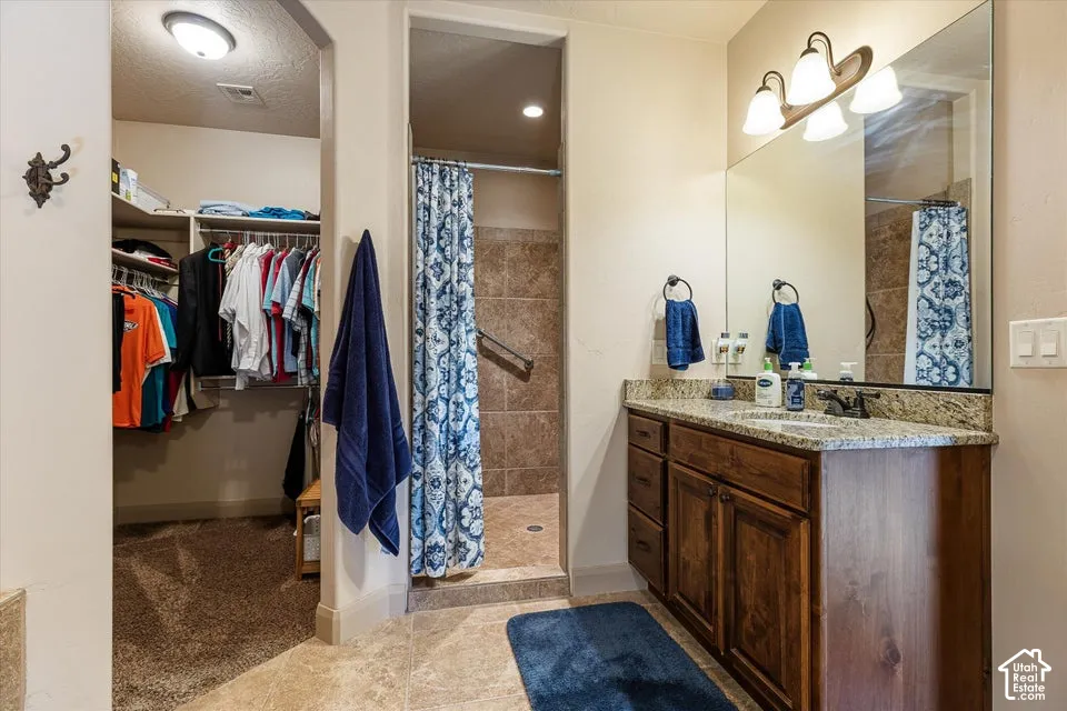 Bathroom featuring a wood-finish vanity with a light granite countertop, an integrated sink, and a large wall-mounted mirror with overhead lighting