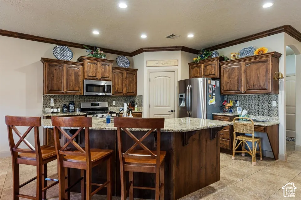 Kitchen featuring wood cabinetry, stainless steel appliances, granite countertops, a center island, and tile flooring