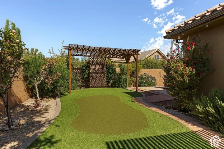 Backyard featuring a putting green, wood pergola, and mature landscaping with a block wall