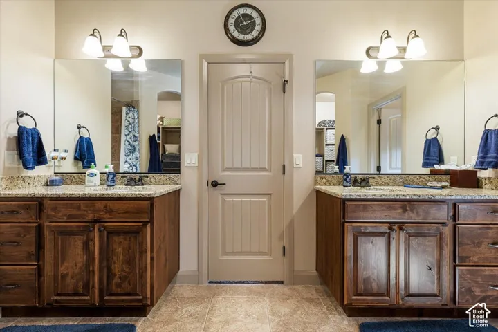 Dual vanity with granite countertops, rich wood-finish cabinetry, and tiled flooring