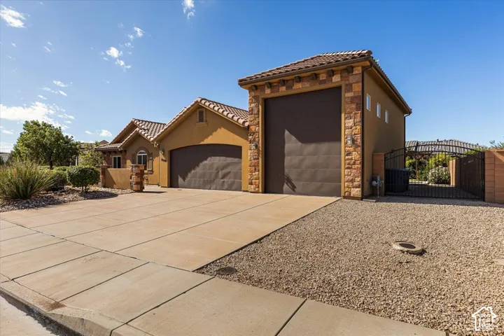 Stucco exterior featuring a tiled roof, multi-car garage, stone accents, and a wrought iron gate