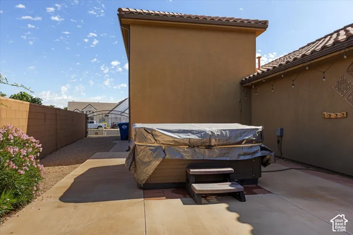 Paved patio area featuring a hot tub with steps, stucco exterior, and tile roofing