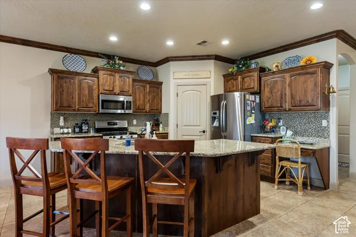 Kitchen featuring wood cabinetry, stainless steel appliances, granite countertops, a center island, and tile flooring