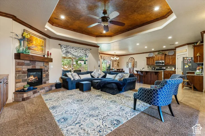 Tray ceiling with wood-finish detailing and recessed lighting, stone-clad fireplace with wood mantle, built-in cabinetry, kitchen island with built-in storage, stainless steel appliances