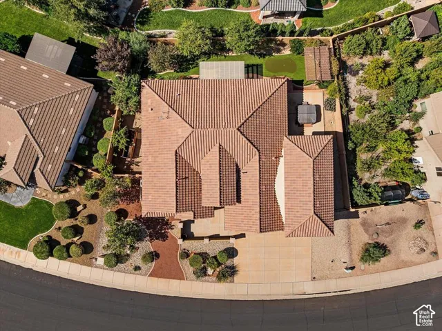 Terracotta tile roof with multiple gables, extensive front yard landscaping featuring manicured shrubs and trees, paved driveway, and additional gravel parking area