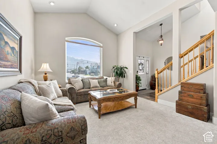 Vaulted ceiling, arched window, carpeted flooring, wood staircase, and a decorative front entry door