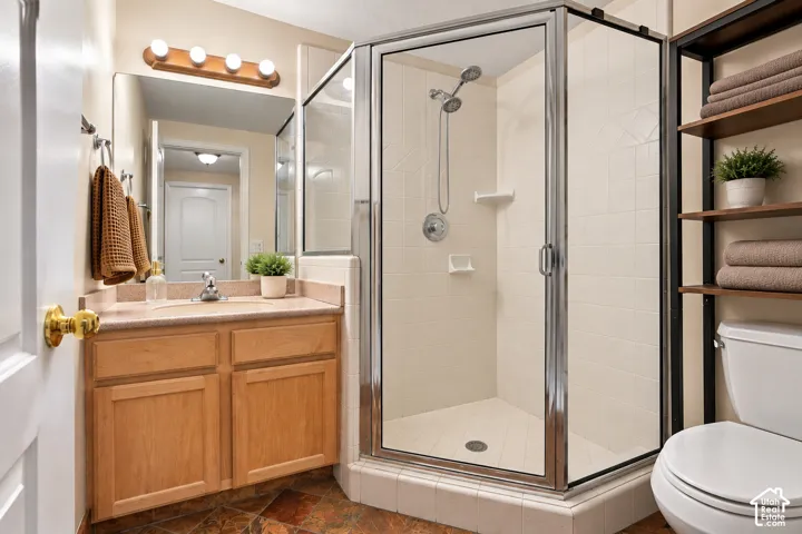 3/4 bathroom featuring a light wood-finish vanity with a single basin sink, a framed mirror, and a glass-enclosed shower with a hand-held showerhead