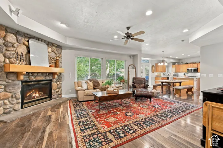 Stone-faced fireplace with a wood mantel, wood-finish flooring, recessed lighting, ceiling fan, and large windows