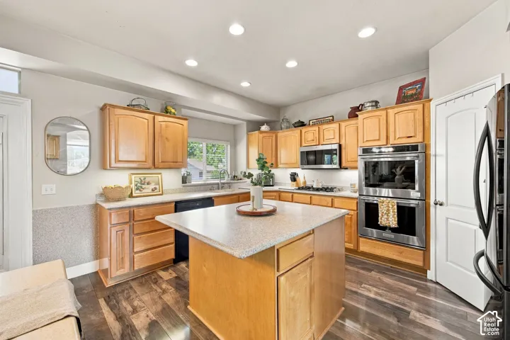 Kitchen featuring wood-finish flooring, recessed lighting, wood cabinetry, a center island with a light-colored countertop, and stainless steel double ovens