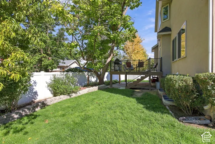 Expansive green lawn with mature trees, retaining wall, white privacy fencing, and an elevated deck with black railings