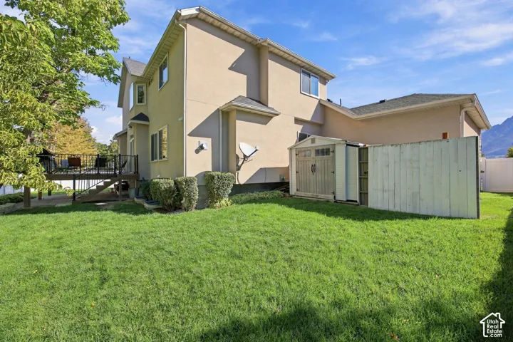 Expansive backyard featuring a manicured lawn, a raised wood deck with dark railings, and a detached storage shed