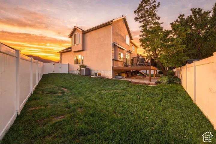 Expansive backyard featuring a manicured lawn, full privacy fencing, and a multi-level deck with stairs to grade