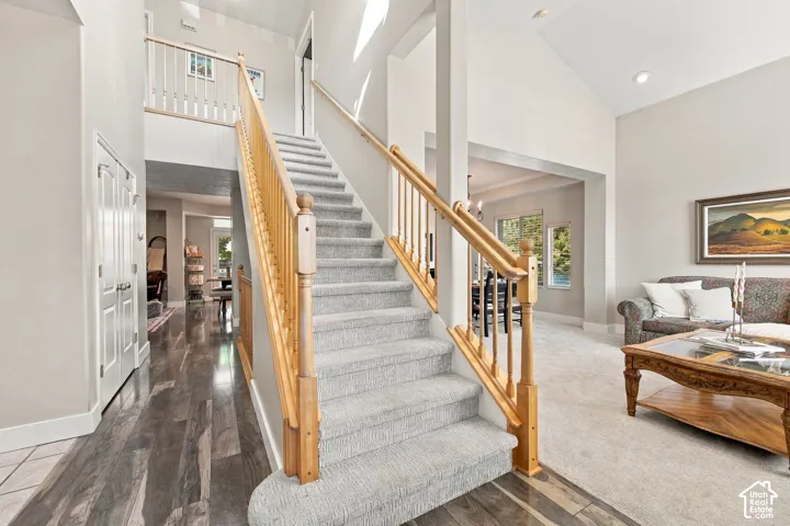 Vaulted ceilings, wood-finish flooring, light-toned carpeting, and a grand staircase with wood railings