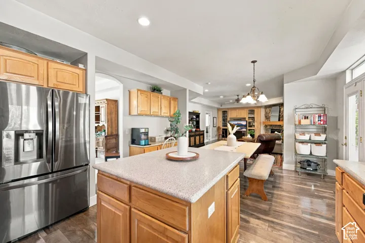 Open-concept kitchen and dining area featuring wood cabinetry, stainless steel appliances including a French-door refrigerator, quartz countertops, a large center island with seating, wood-finish flooring, and recessed lighting throughout