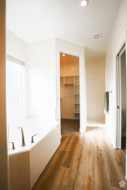 Soaking tub with brushed nickel fixtures, wood-finish flooring, recessed lighting, and a walk-in closet with built-in shelving