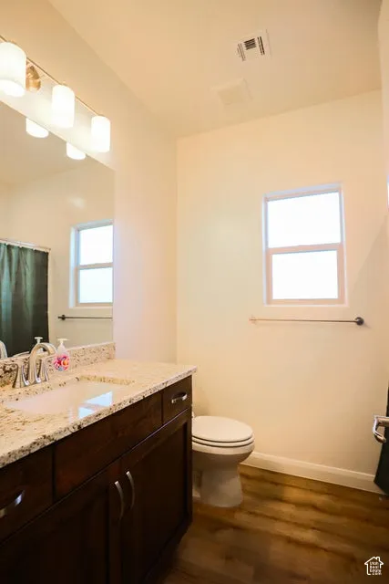 Wood-finish flooring, dark wood-tone vanity with dual cabinet doors and drawers, light granite-style countertop with an undermount sink, and a multi-bulb vanity light fixture