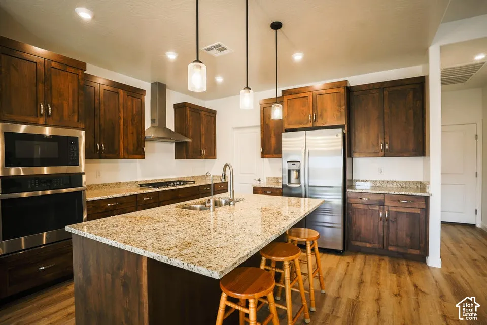 Kitchen featuring rich wood cabinetry, stainless steel appliances, speckled granite countertops, a central island with a sink, and wood-finish flooring