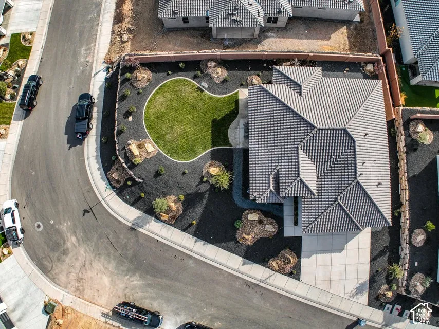 Pitched tile roof with multiple gables, extensive dark rock landscaping, manicured lawn feature, concrete driveway, and concrete sidewalk