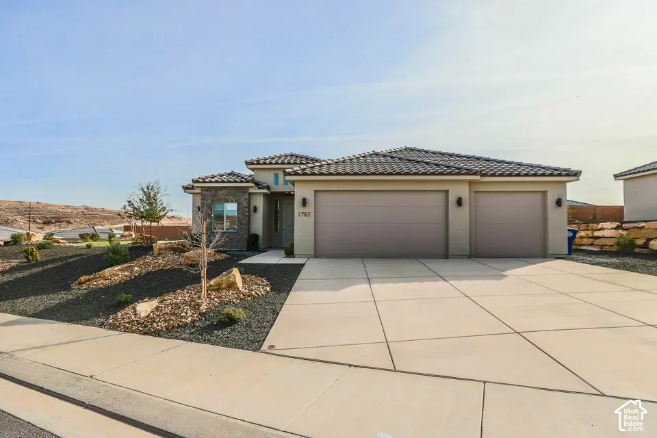 Stucco exterior with stone accents, tile roof, three-car garage, concrete driveway, and desert-style landscaping